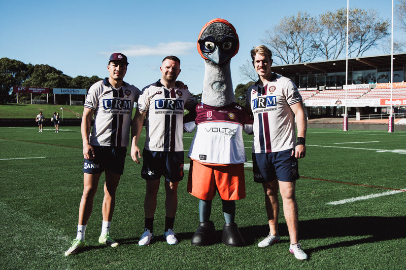 VoltX Energy mascot Eddie wearing a Sea Eagles jersey with three Manly Sea Eagles players on the field at 4 Pines Park